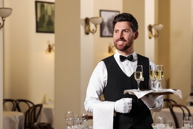 Photo of Butler holding tray with glasses of sparkling wine in restaurant. Space for text