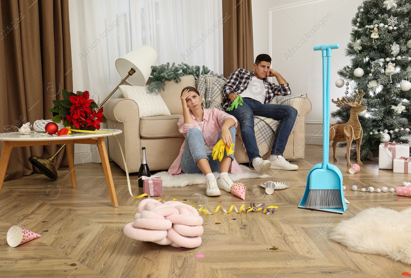 Photo of Tired couple sitting in messy room while cleaning after New Year party