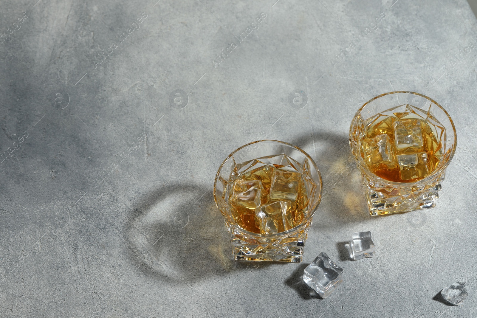 Photo of Whiskey in glasses with ice cubes on grey textured table, above view. Space for text