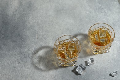 Whiskey in glasses with ice cubes on grey textured table, above view. Space for text