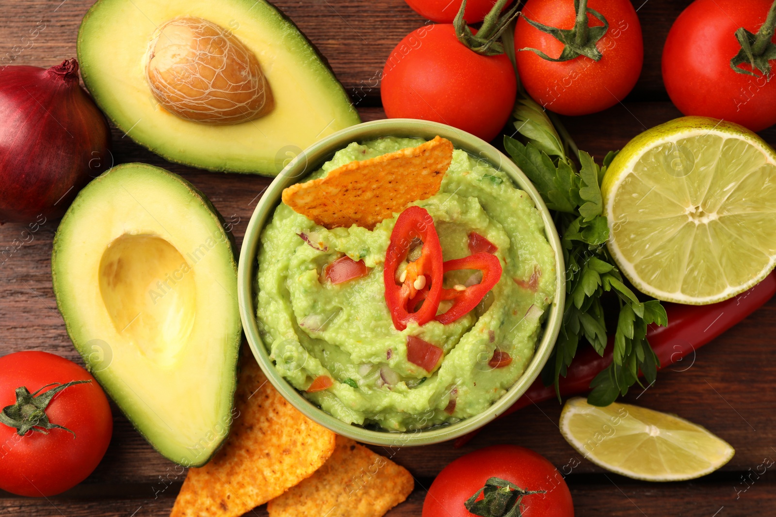 Photo of Bowl of delicious guacamole, nachos chips and ingredients on wooden table, flat lay