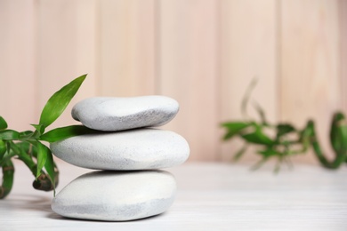 Photo of Spa stones and bamboo leaves on table against blurred background. Space for text