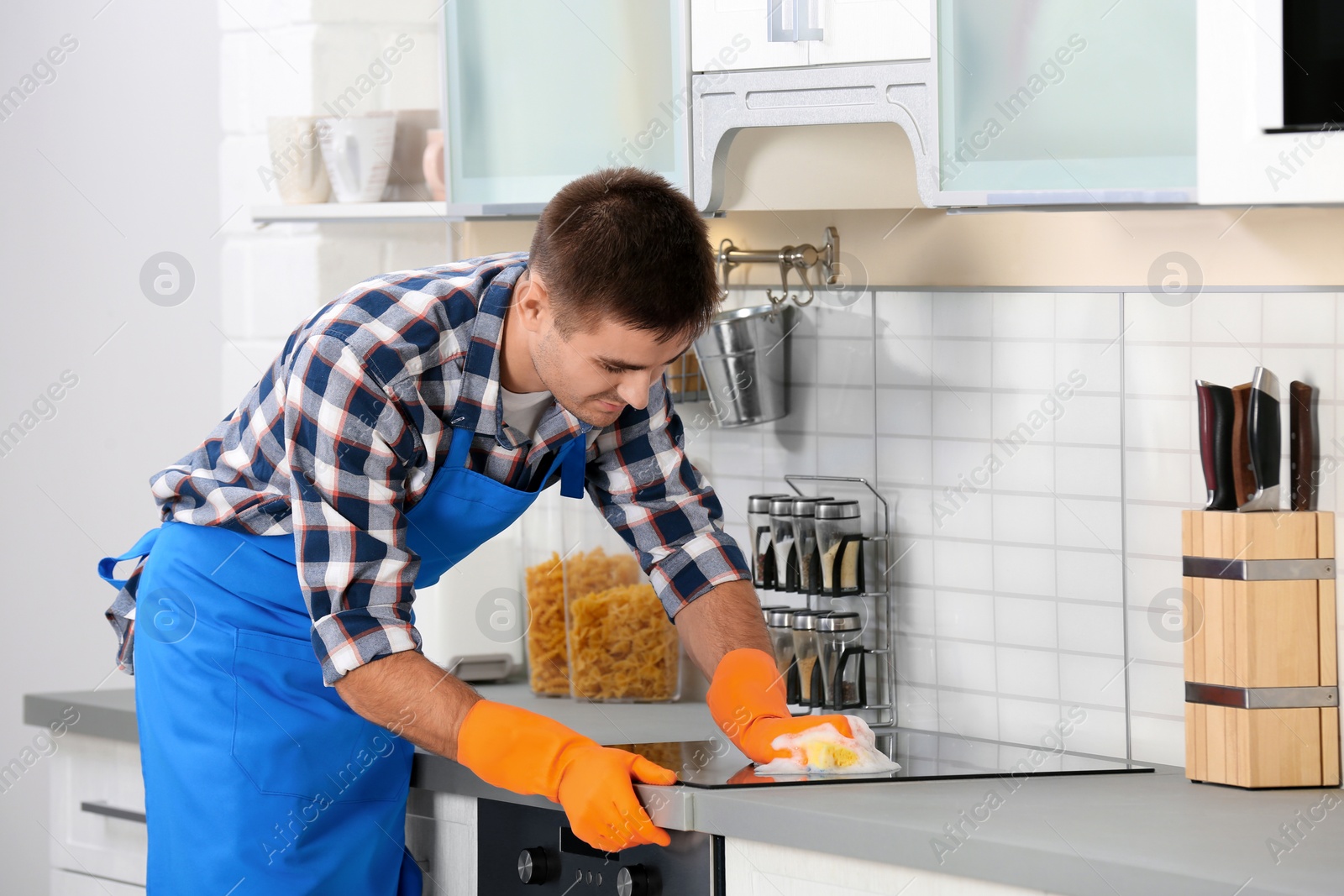 Photo of Man cleaning kitchen stove with sponge in house