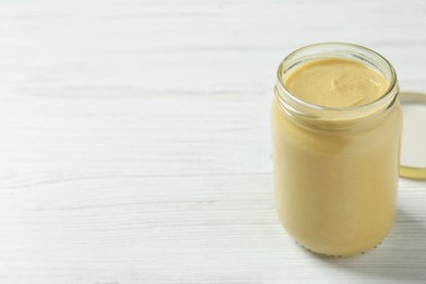 Photo of Spicy mustard in glass jar on white wooden table. Space for text