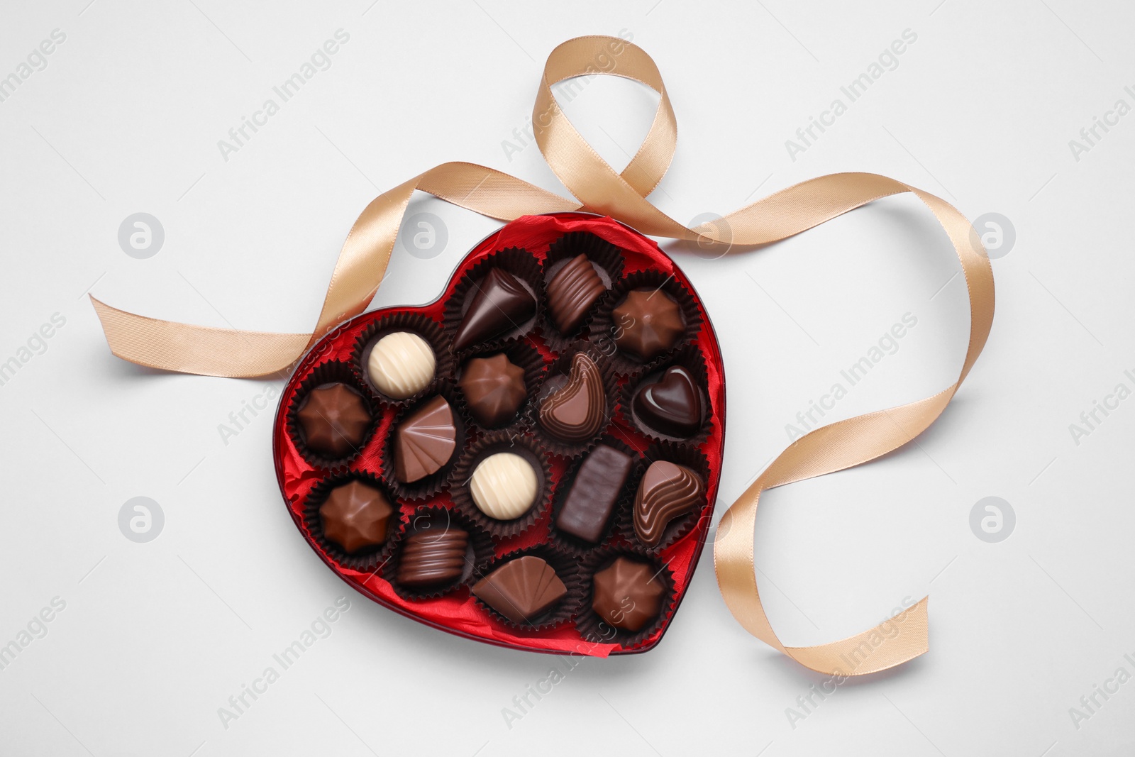 Photo of Heart shaped box with delicious chocolate candies and ribbon on white background, top view