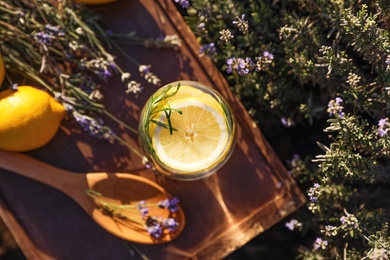 Photo of Glass of fresh lemonade on wooden tray in lavender field, top view