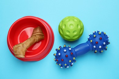 Pet toys, bowl with dog treat on light blue background, flat lay
