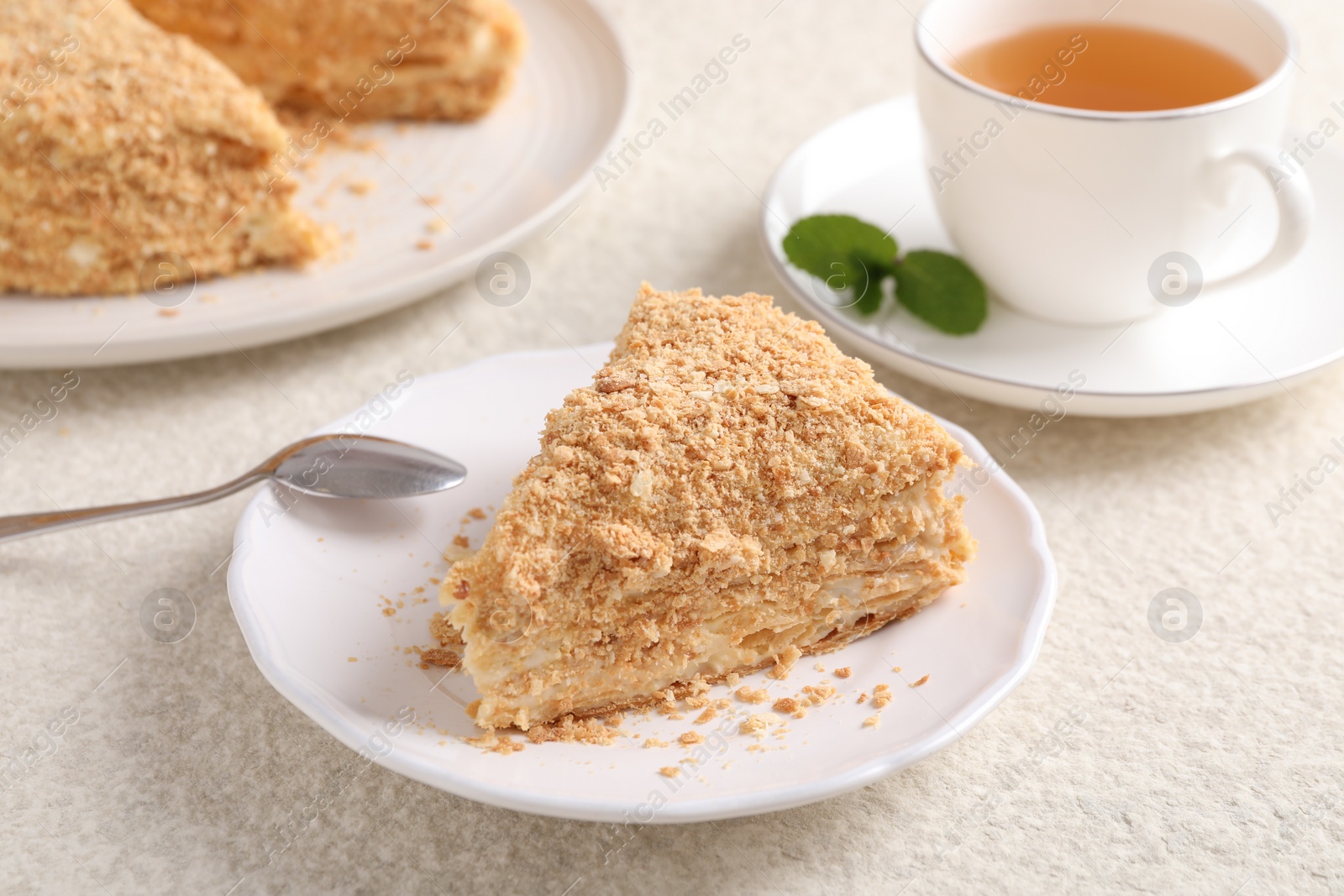 Photo of Piece of delicious Napoleon cake served on beige table, closeup