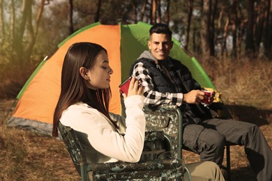 Photo of Couple resting in camping chairs and enjoying hot drink outdoors