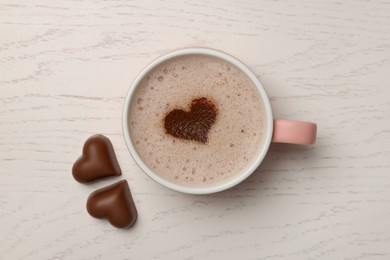 Photo of Cup of aromatic coffee with heart shaped decoration and chocolate candies on white wooden table, flat lay
