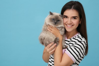 Happy woman with her cute cat on light blue background, space for text