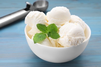 Delicious vanilla ice cream and mint in bowl on light blue wooden table, closeup