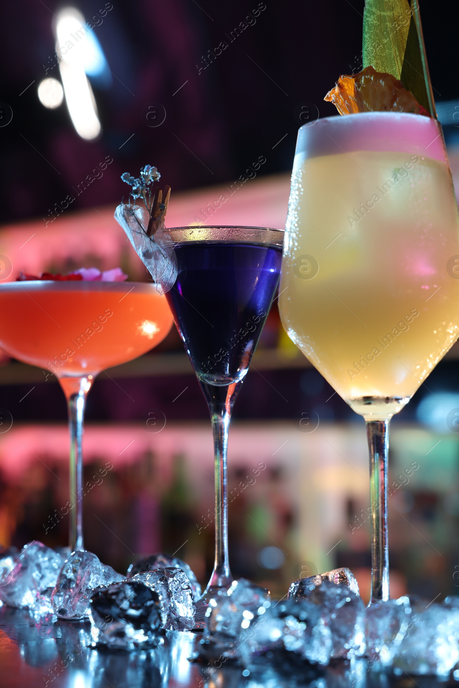 Photo of Different fresh alcoholic cocktails and ice cubes on counter in bar