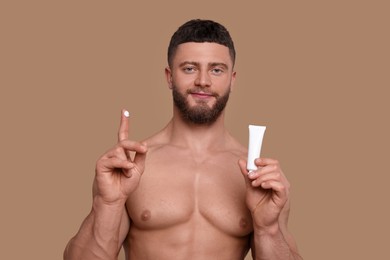 Photo of Handsome man with tube of body cream on pale brown background