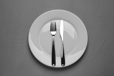Photo of Empty plate and cutlery on grey textured table, top view