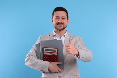 Photo of Happy accountant with calculator and folders showing thumb up on light blue background