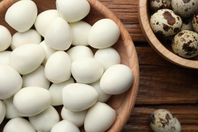 Photo of Unpeeled and peeled boiled quail eggs on wooden table, flat lay