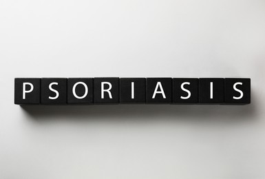 Photo of Word Psoriasis madeblack wooden cubes with letters on light grey background, top view