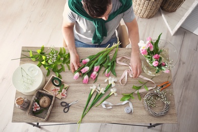 Male decorator creating beautiful bouquet at table, top view