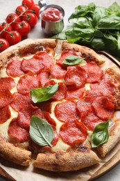 Tasty pepperoni pizza with basil, sauce and tomatoes on table