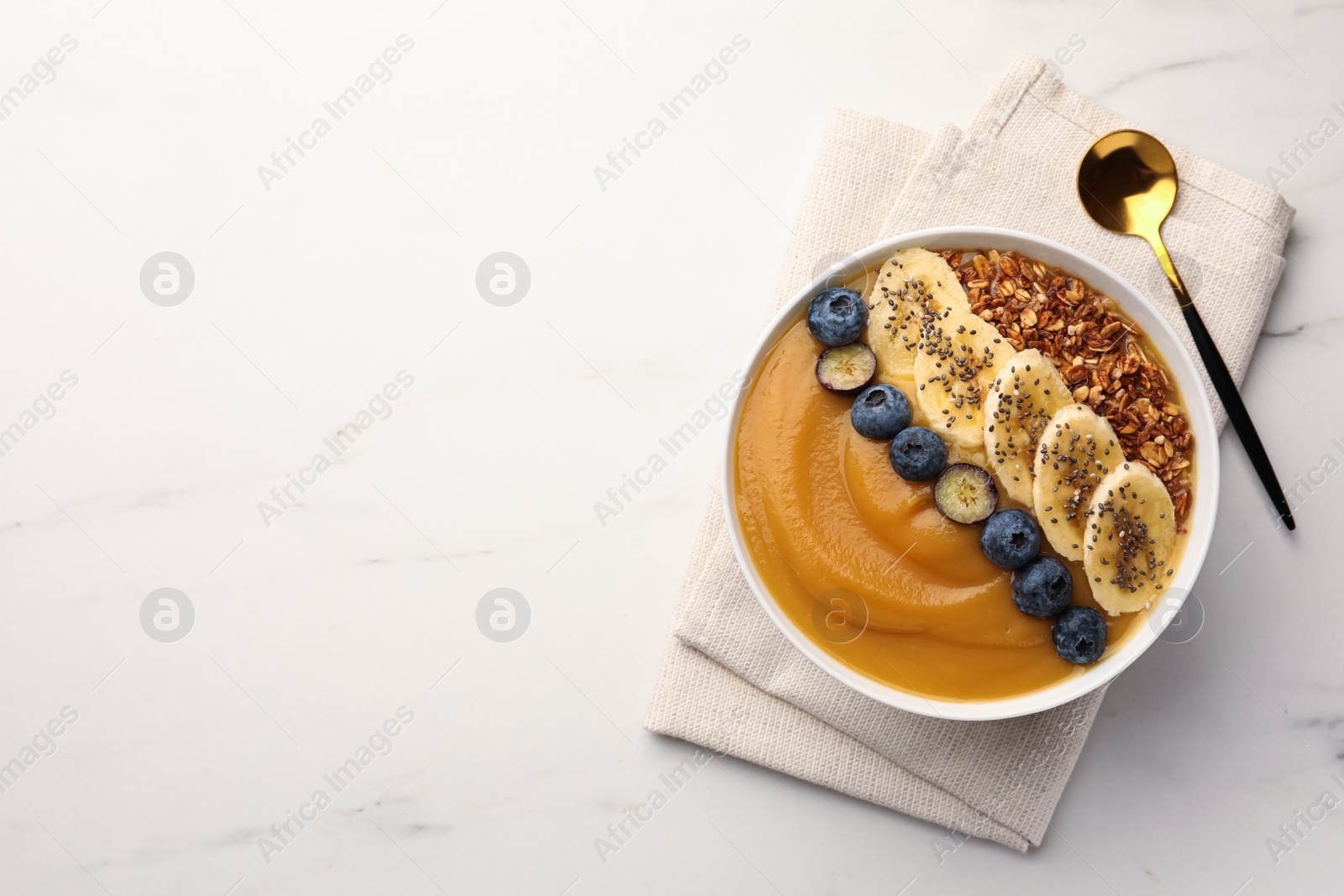 Photo of Delicious smoothie bowl with fresh blueberries, banana and granola on white marble table, flat lay. Space for text