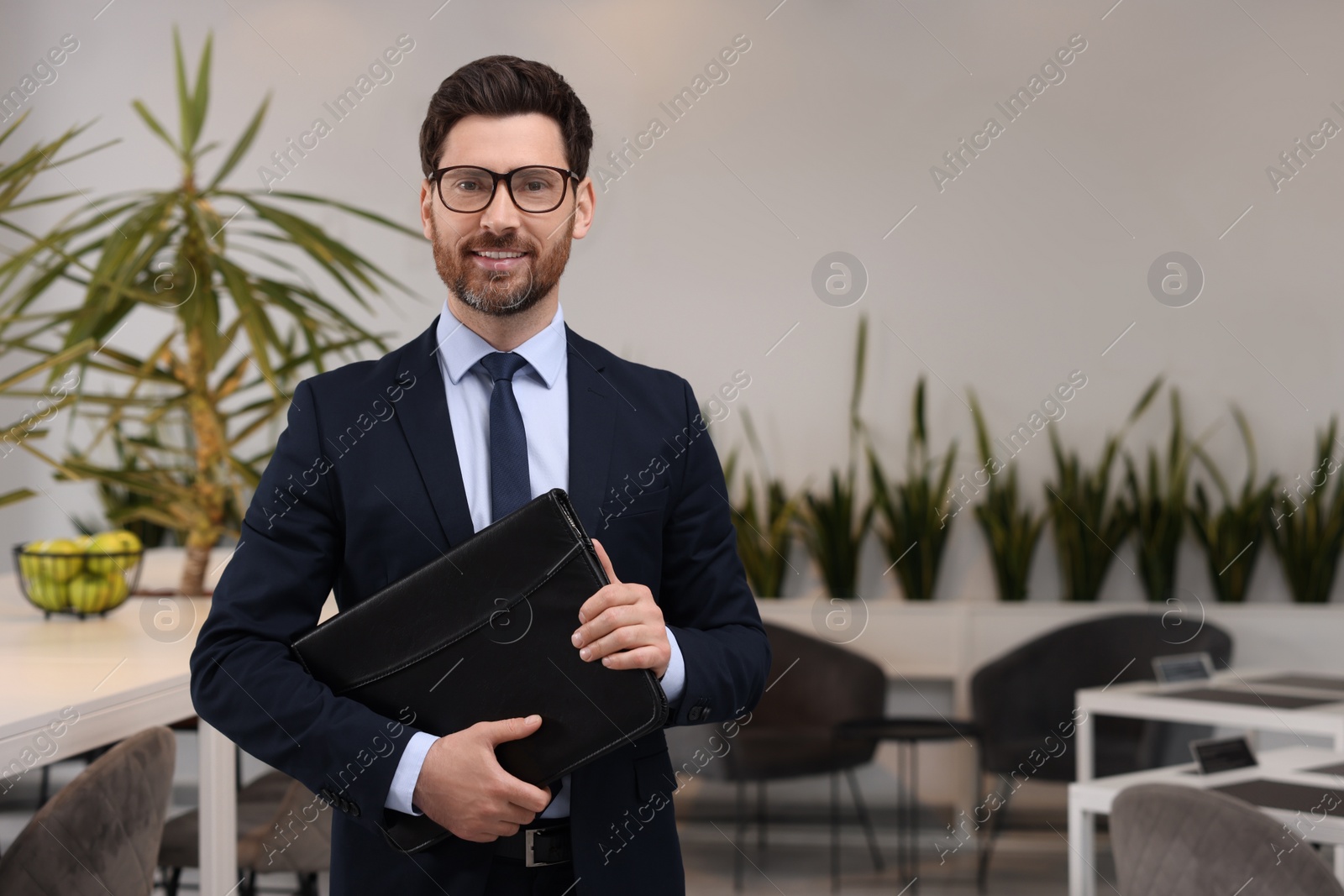 Photo of Happy real estate agent with leather portfolio indoors. Space for text