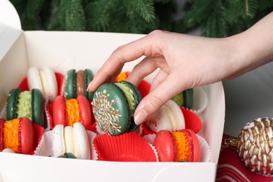 Woman with box of decorated Christmas macarons at table, closeup