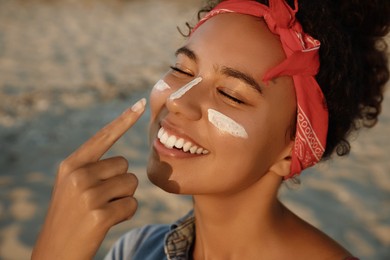Photo of Happy African American woman with sun protection cream on face at beach, closeup