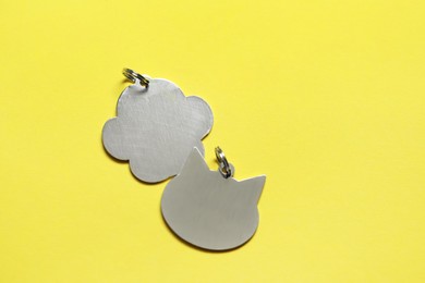 Silver pet tags on yellow background, flat lay. Space for text