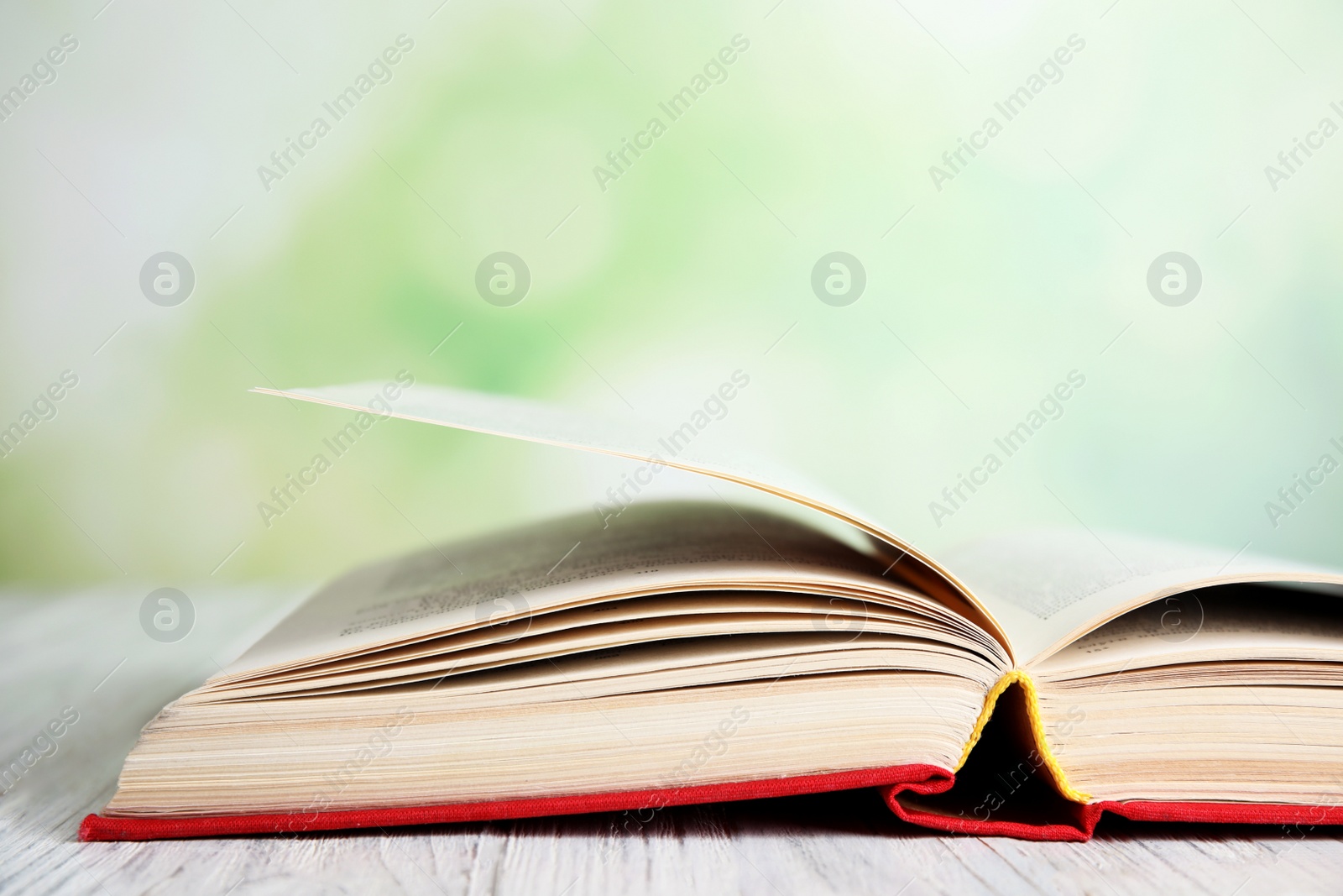 Photo of Open book on white wooden table against blurred green background, closeup. Space for text