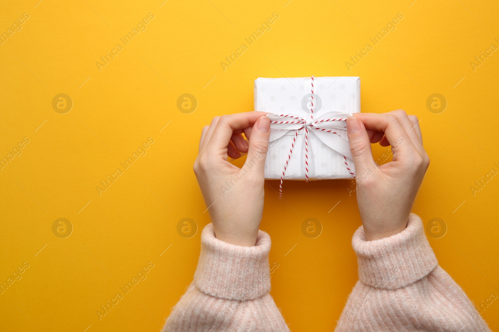 Photo of Woman holding Christmas gift box on orange background, top view