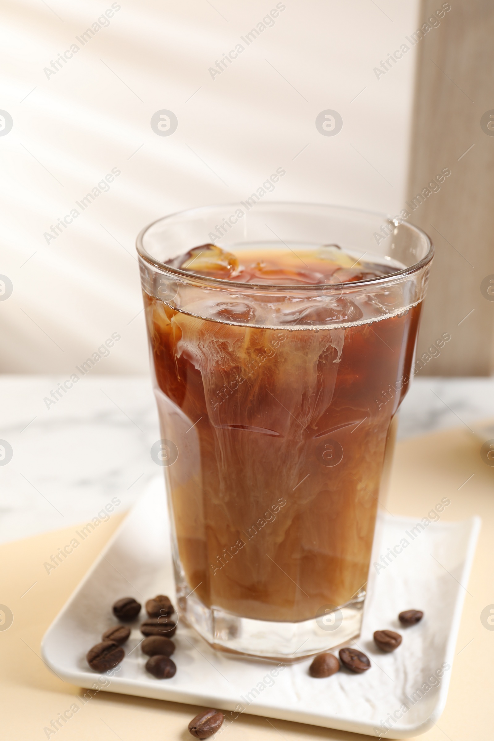 Photo of Refreshing iced coffee with milk in glass and beans on beige table