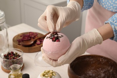 Photo of Woman in gloves making bath bomb at white table indoors, closeup