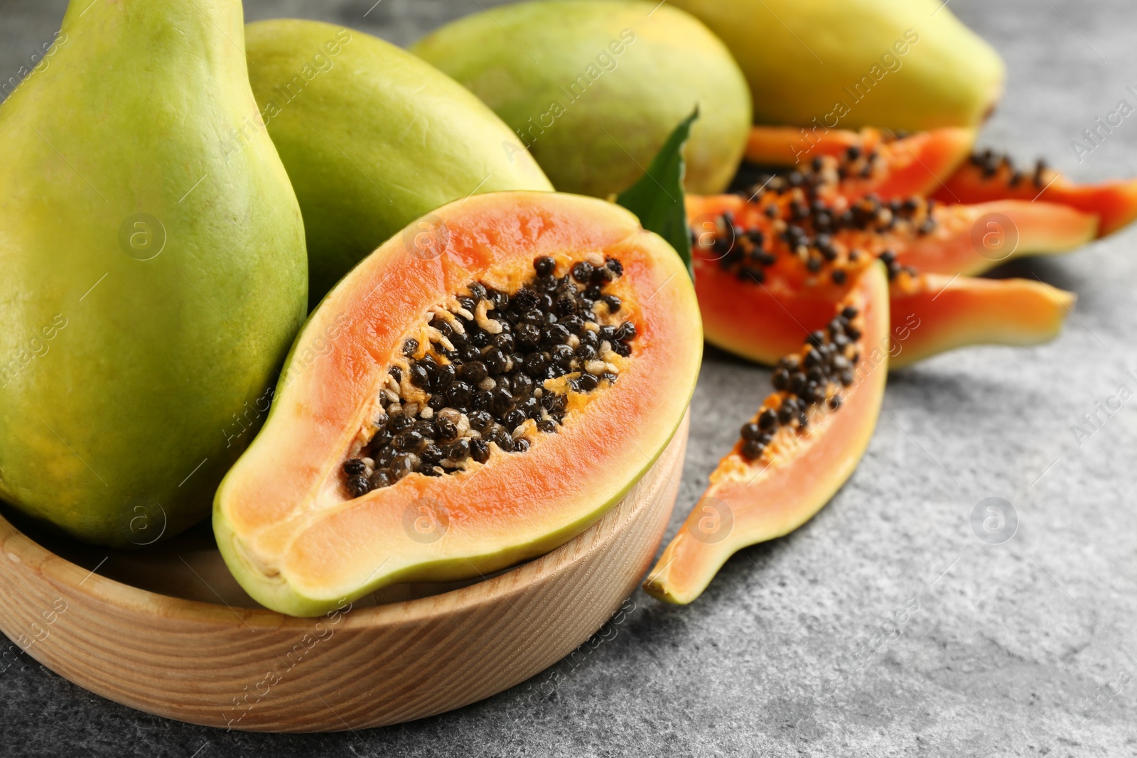 Photo of Fresh ripe papaya fruits in wooden bowl on grey table