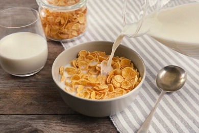 Photo of Pouring milk into bowl with healthy cornflakes on table