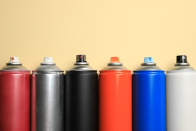 Photo of Cans of different spray paints on beige background, flat lay with space for text. Graffiti supplies