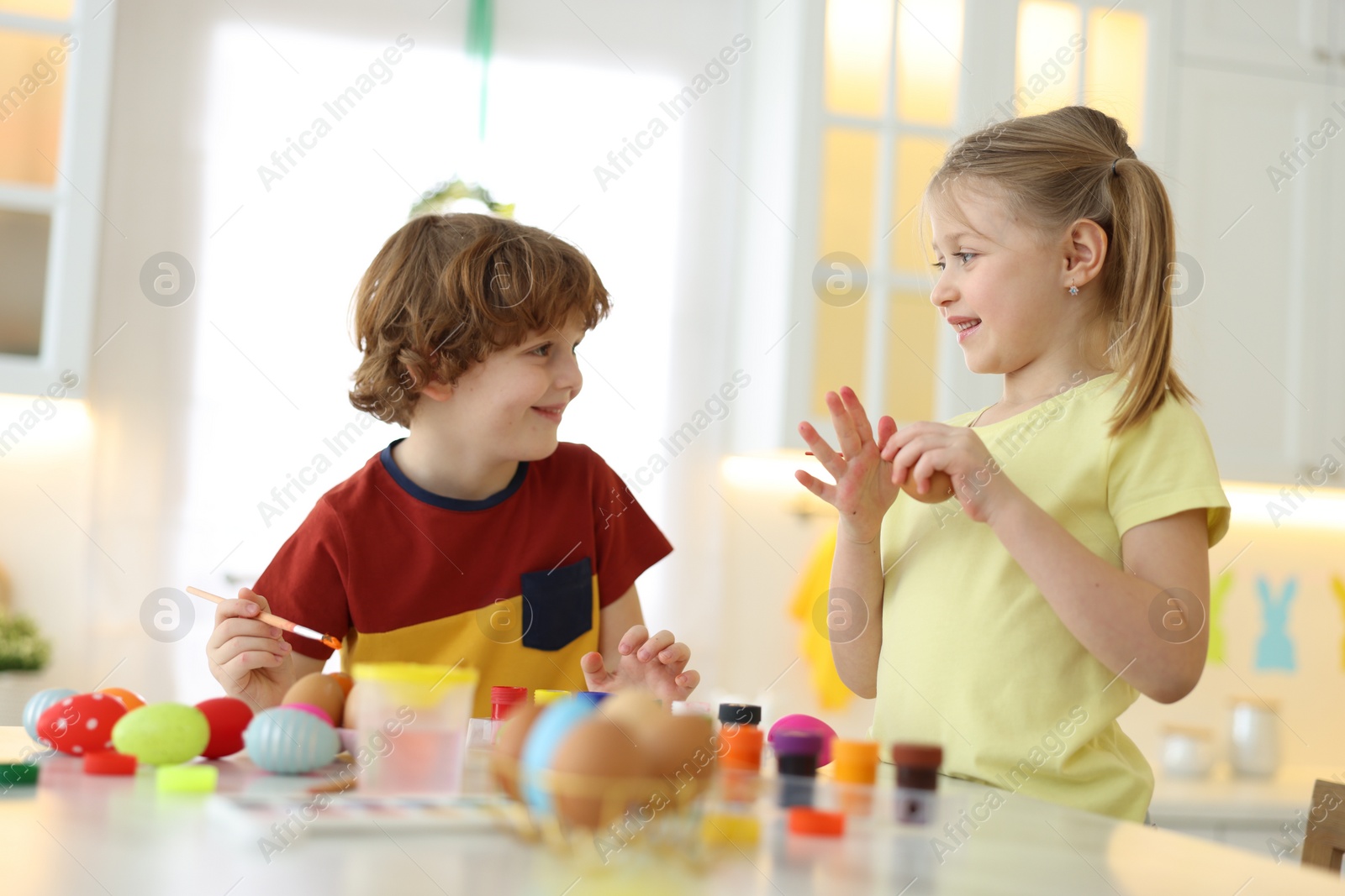 Photo of Easter celebration. Cute children painting eggs at white table in kitchen