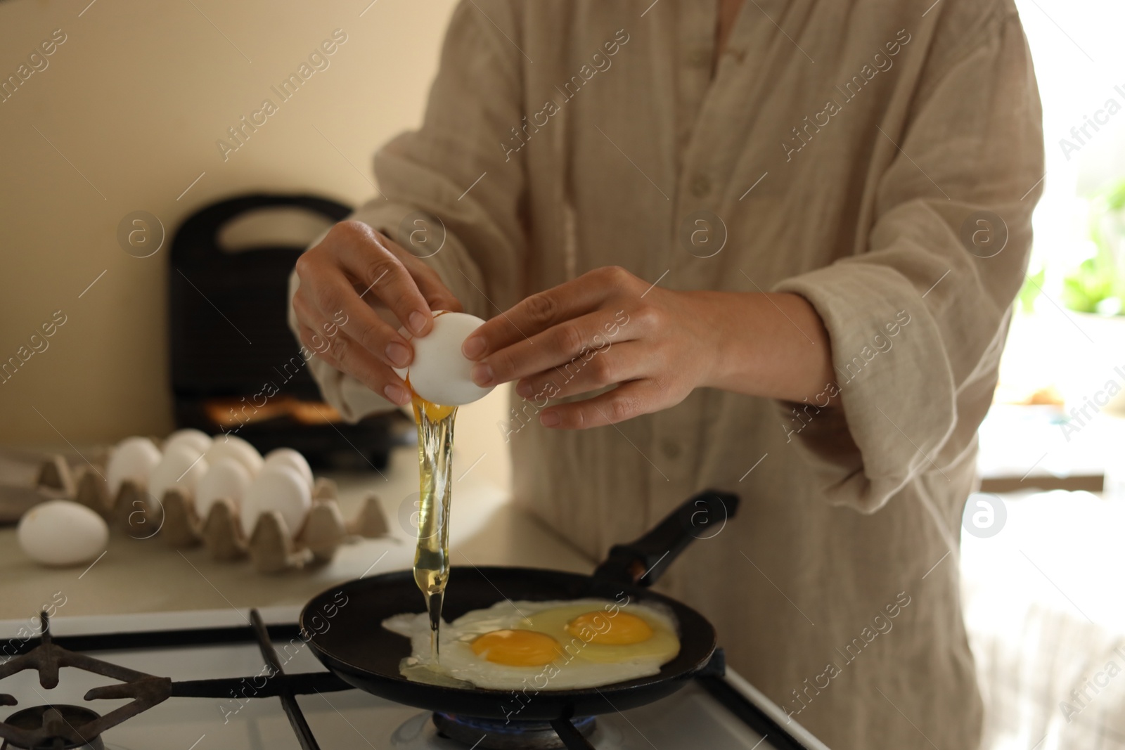 Photo of Woman cooking tasty eggs on frying pan in kitchen, closeup