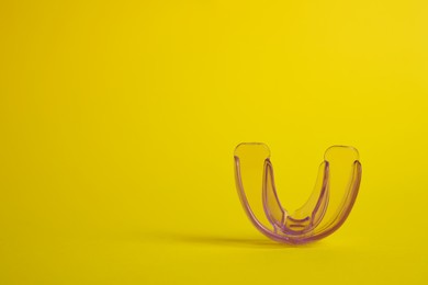 Photo of Transparent dental mouth guard on yellow background, space for text. Bite correction