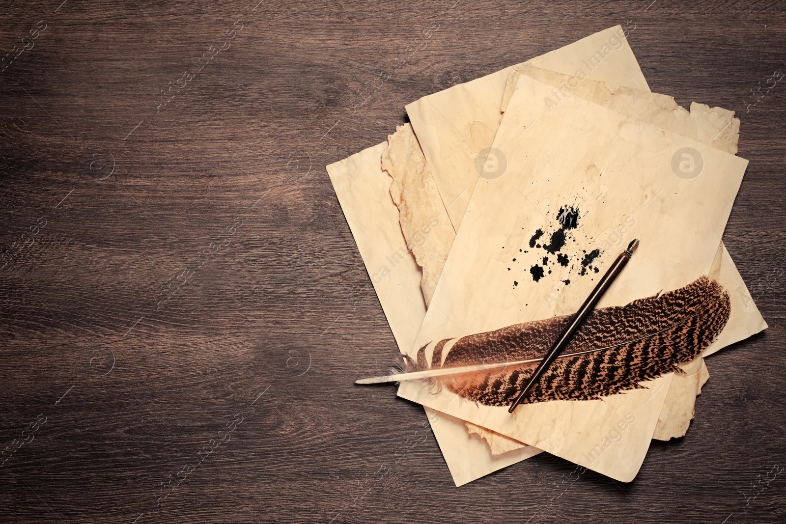 Photo of Feather, fountain pen and vintage parchment with ink stains on wooden table, top view. Space for text