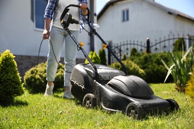 Woman cutting green grass with lawn mower in garden, closeup