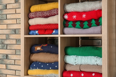 Photo of Folded winter clothes on shelves near brick wall