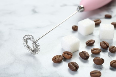 Photo of Pink milk frother wand, sugar cubes and coffee beans on white marble table, closeup