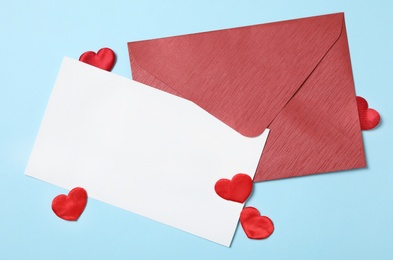 Photo of Blank card, envelope and decorative hearts on light blue background, flat lay with space for text. Valentine's Day celebration