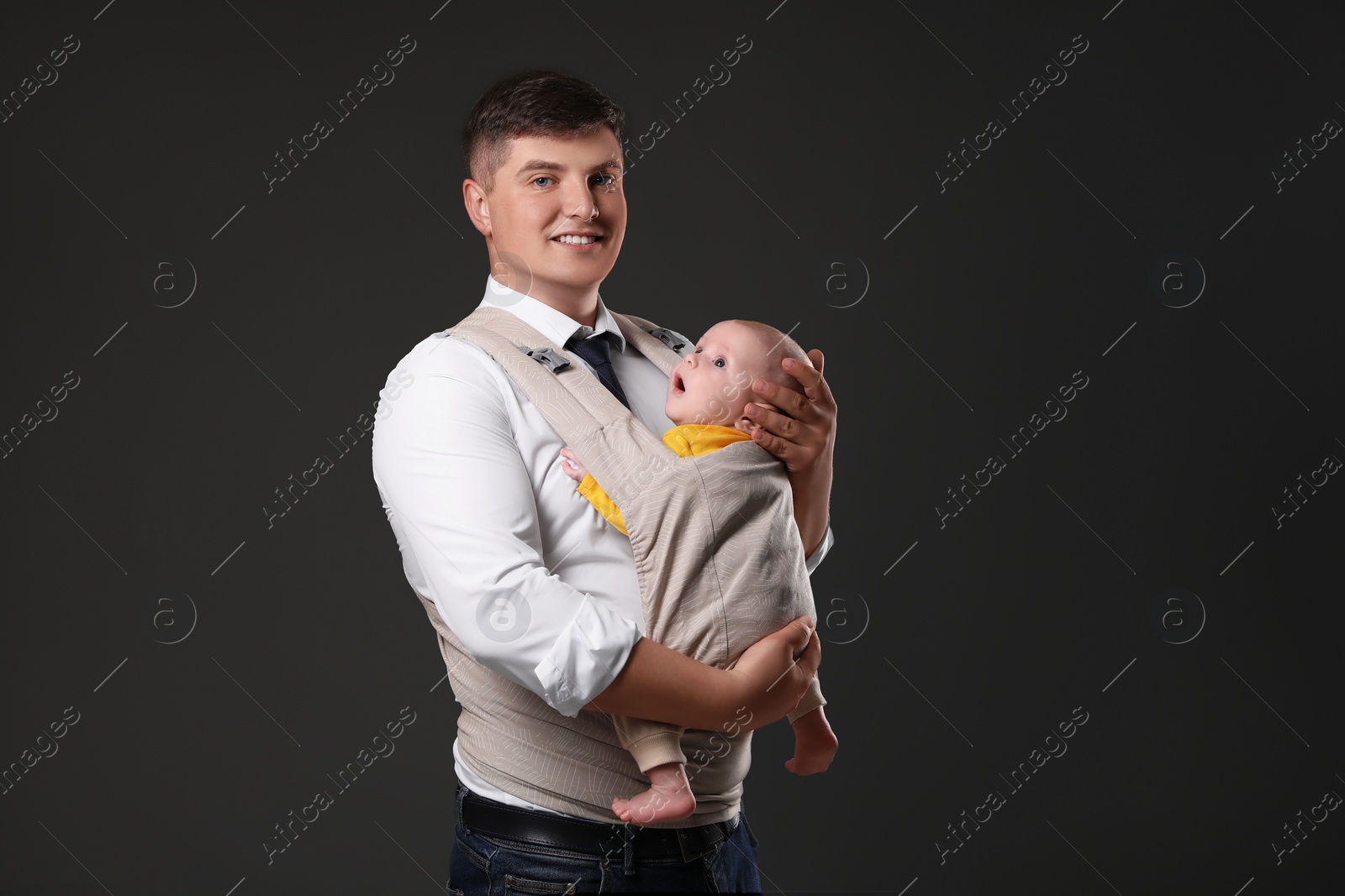 Photo of Father holding his child in baby carrier on black background