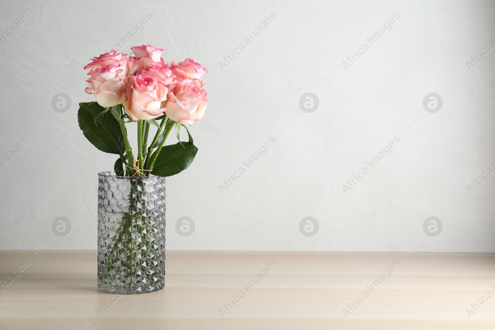 Photo of Vase with beautiful pink roses on wooden table. Space for text