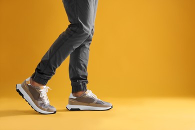 Photo of Man walking in sneakers on yellow background, closeup. Space for text