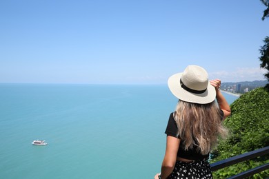 Photo of Woman with hat near sea on sunny day, back view. Space for text