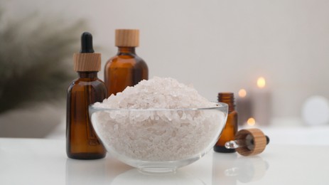 Photo of Glass bowl with bath salt and cosmetic products on white countertop indoors, closeup