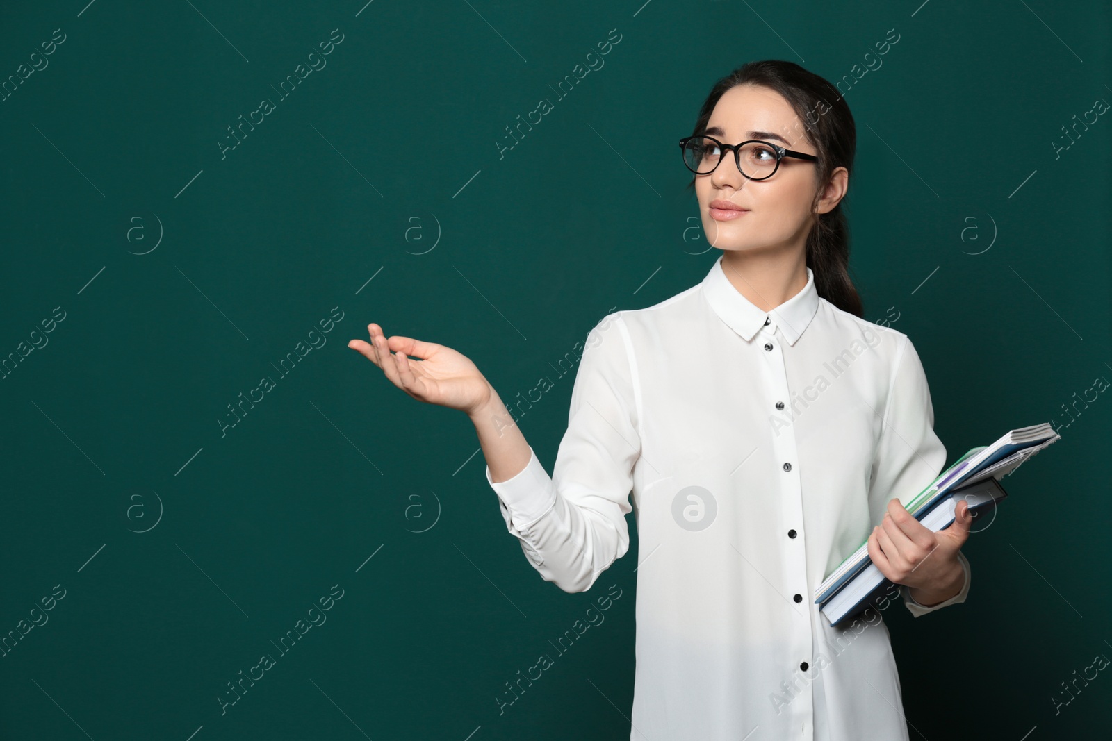 Photo of Portrait of beautiful young teacher with books near chalkboard, space for text